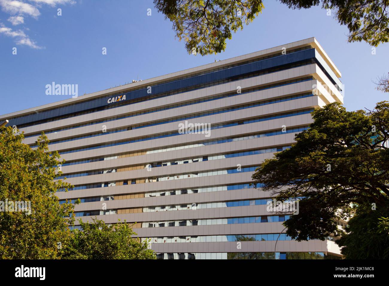 Brasília, Federal District, Brasilien – 23. Juli 2022: Fassade der brasilianischen Bank Caixa Econômica Federal, zwischen Bäumen, an einem klaren Tag mit blauem Himmel. Stockfoto