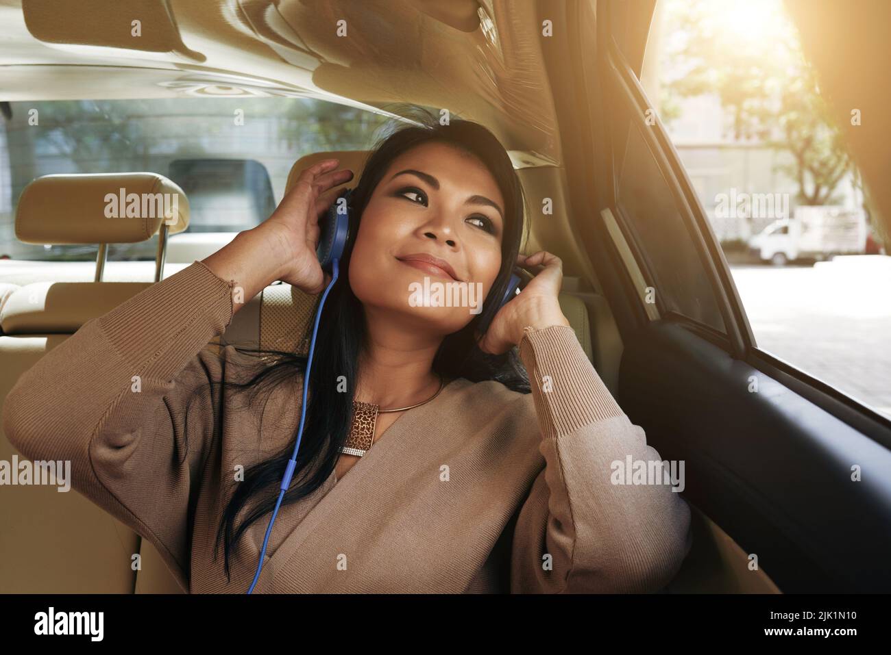 Schöne vietnamesische Frau, die im Auto sitzt und ihrer Lieblingsmusik lauscht Stockfoto
