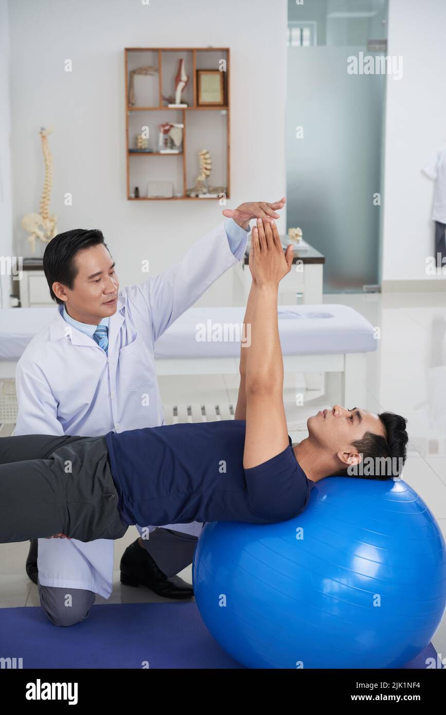 Vietnamesischer Physiotherapeut, der mit einem jungen Patienten in seinem Büro arbeitet Stockfoto