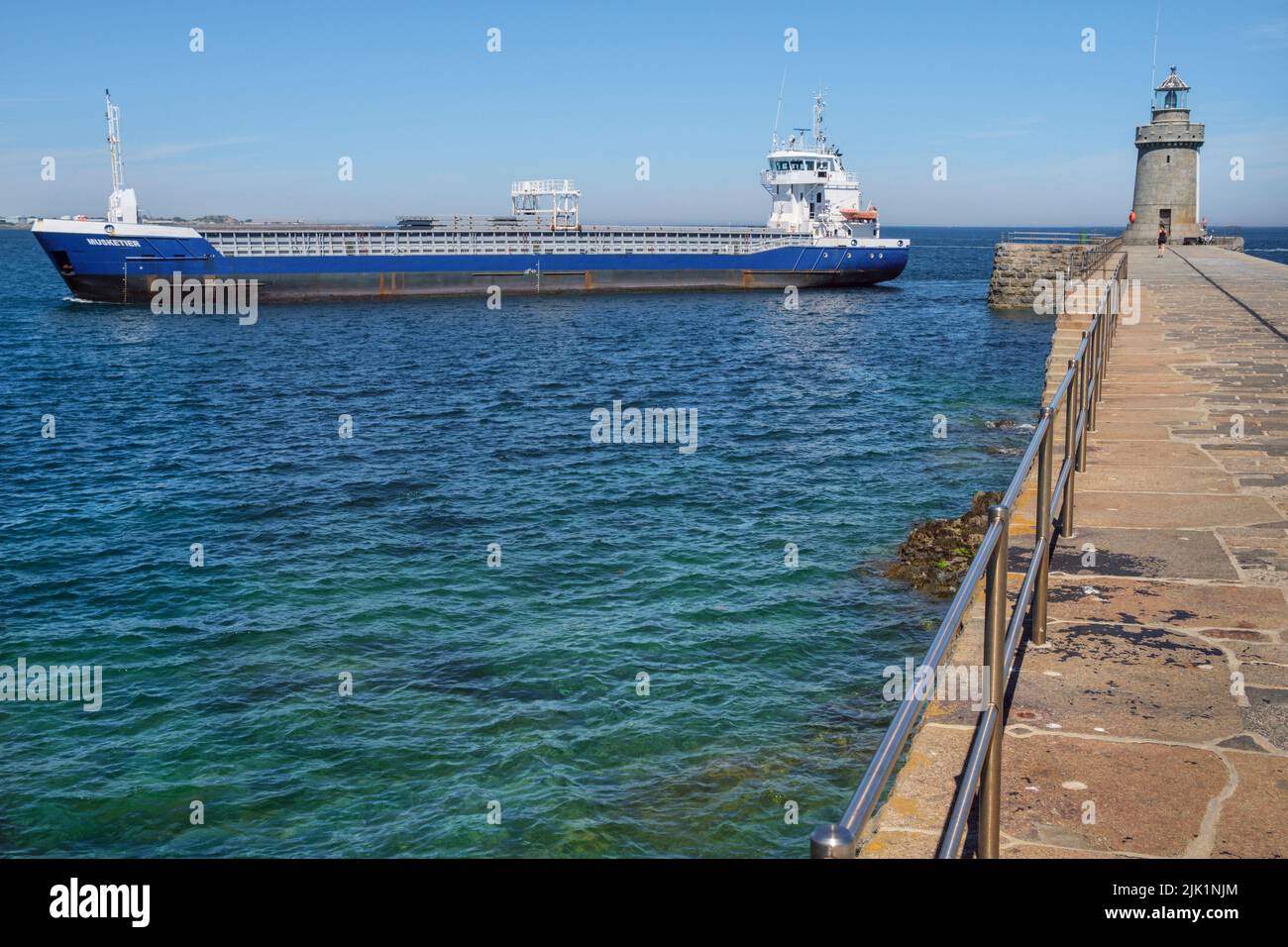 Ein Frachtschiff passiert den Leuchtturm am White Rock Pier, um in den Hafen von St. Peter Port, Guernsey, Channel Islands zu gelangen Stockfoto