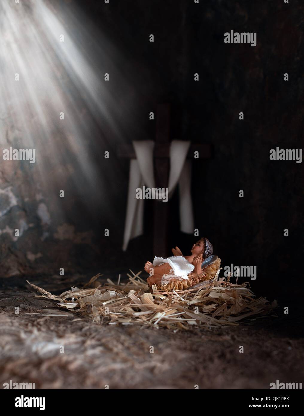 Weihnachtszeit. Jesuskind in einer Krippe, Lichtstrahlen, die ihn mit Holzkreuz im Hintergrund leuchten. Stockfoto