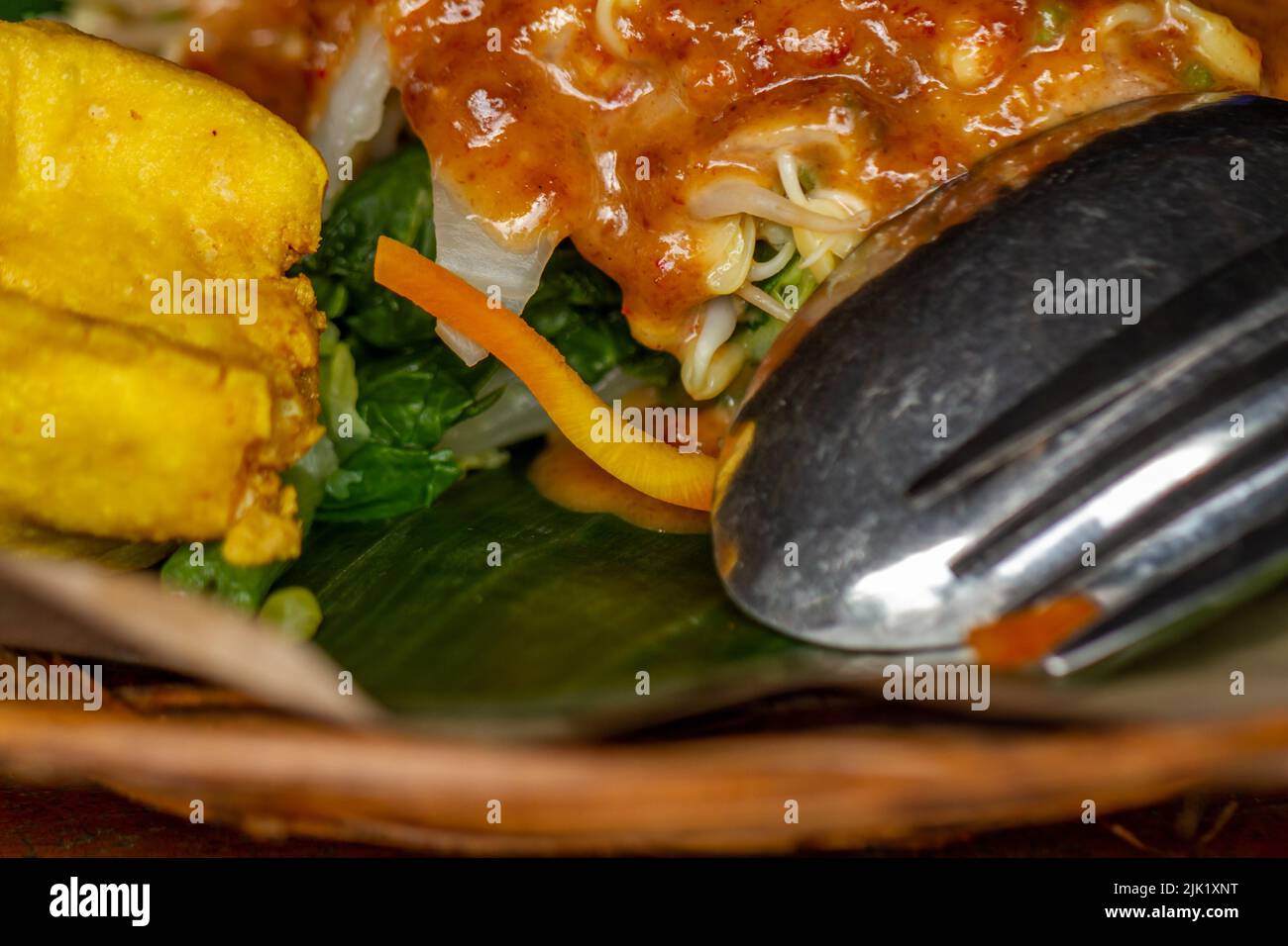 Javanesischer Salat aus frischem Gemüse und Gewürzen aus Erdnüssen, serviert auf einem Teller aus gewebtem Rattan Stockfoto