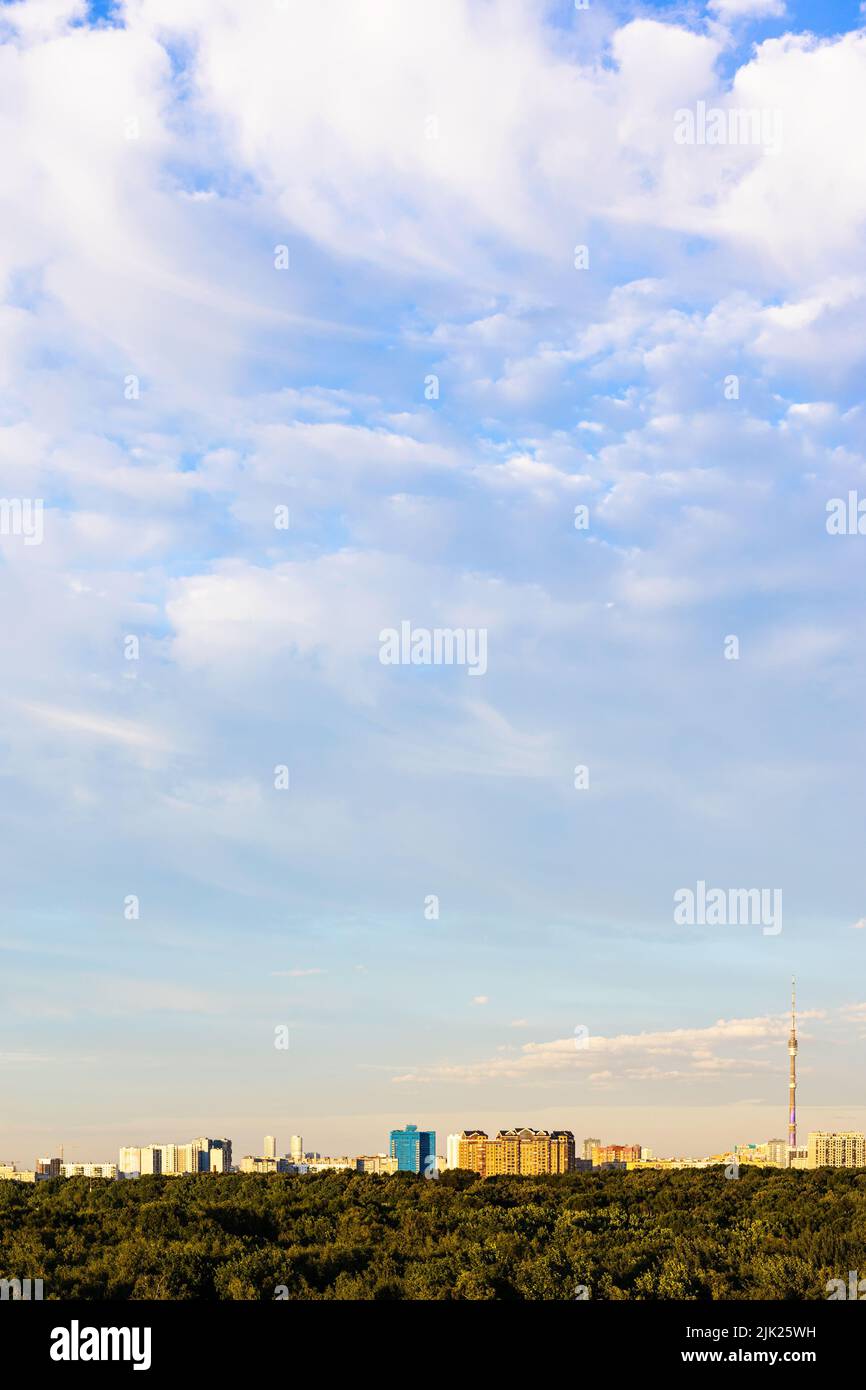 Weiße Wolken am blauen Himmel über dem Stadtpark und den Wohnhäusern am Horizont bei Sonnenuntergang im Sommer Stockfoto