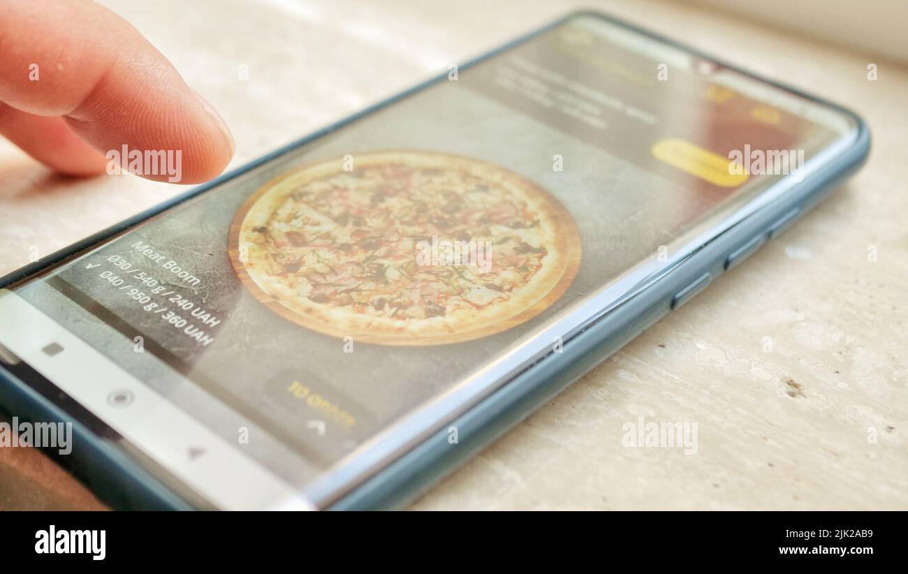 Der Prozess der Auswahl und Bestellung von Takeaway Food Pizza Online in der mobilen App über ein Telefon. Nahaufnahme des Smartphone-Bildschirms und männlicher Finger Stockfoto