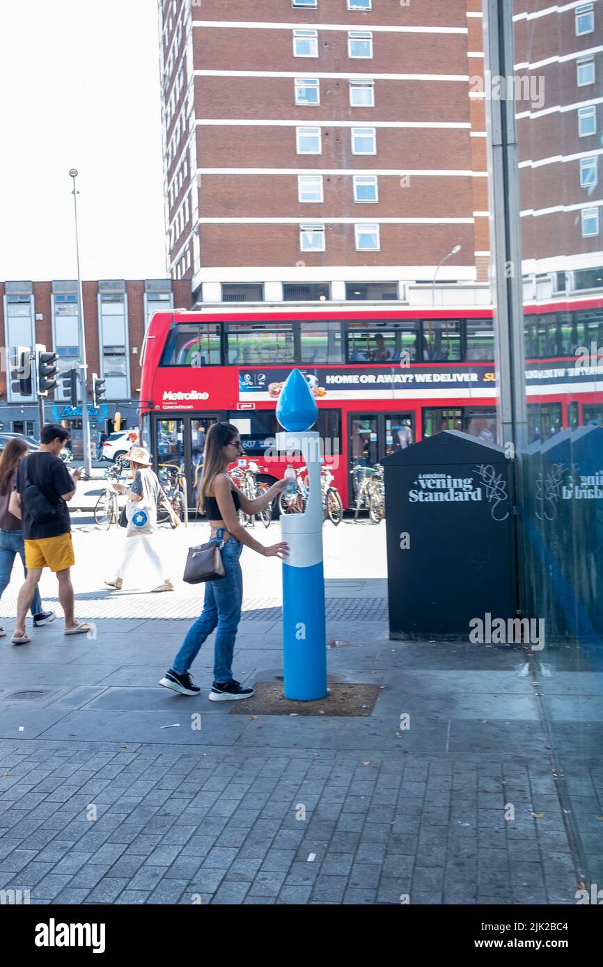 London, 2022. Juli: Eine Frau füllt eine wiederverwendbare Wasserflasche an einem Brunnen in Shepherds Bush Stockfoto