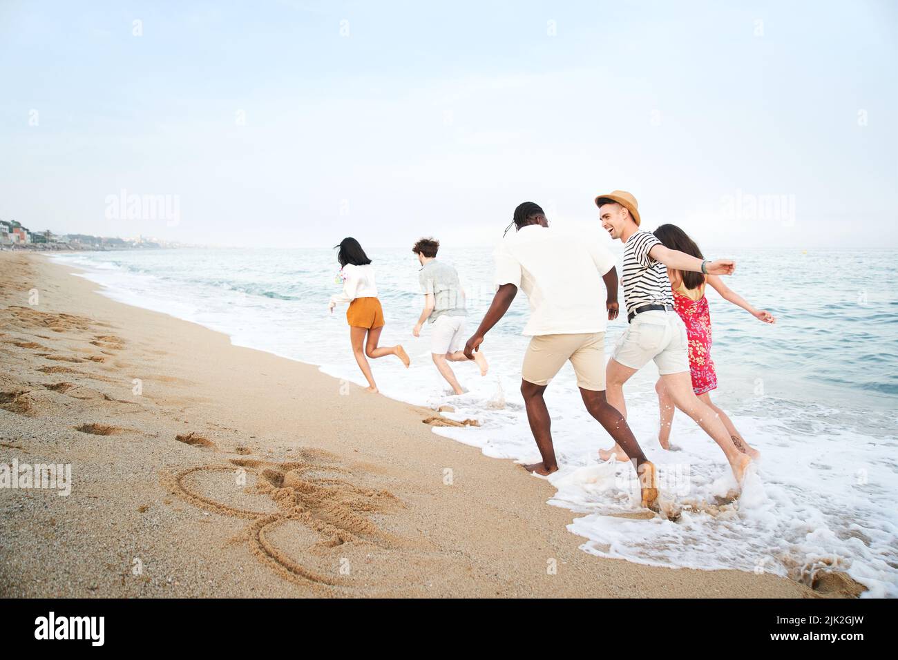 Fröhliche junge Freunde Gruppe haben Spaß feiern beim Springen und Laufen am Strand bei Sonnenuntergang Stockfoto