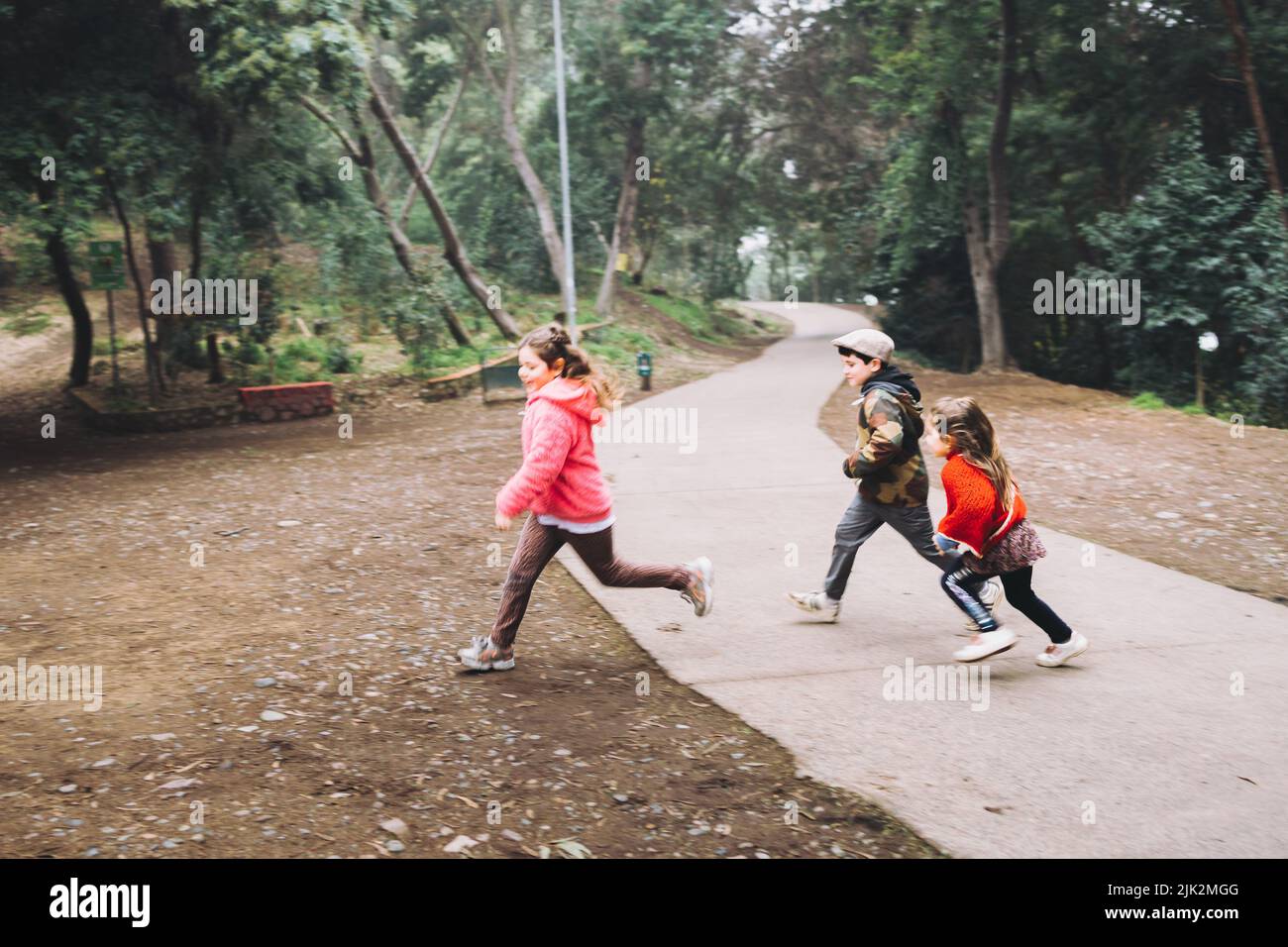 Drei Kinder, zwei Mädchen und ein Junge, die auf einer Parkstraße spielen, lachen und Rennen. Stockfoto