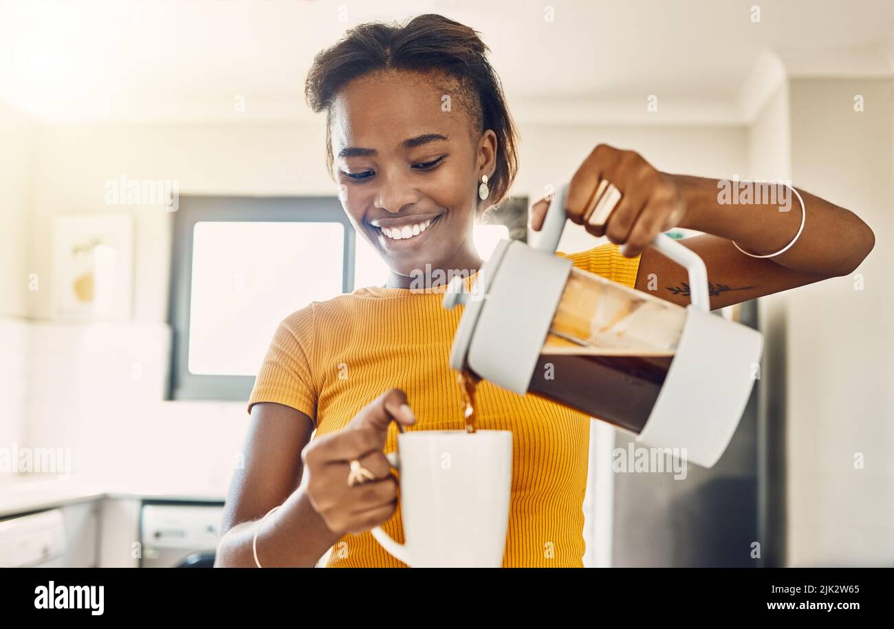 Schöne, glückliche und entspannte Frau, die Kaffee macht und heiße Getränke in die Tasse gießt, um morgens die Hausküche zu genießen. Junge lächelnde Dame bereitet oder vor Stockfoto
