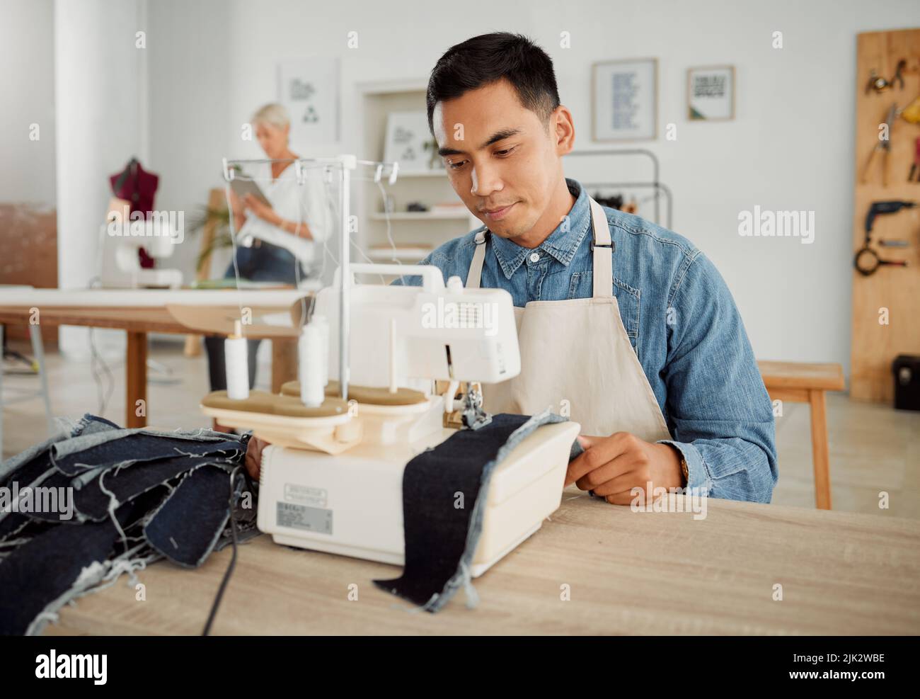 Mode, Design und Stil mit einem jungen Designer, der in einem Startup an einer Nähmaschine in einer Werkstatt arbeitet. Viel beschäftigter und kreativer Designer, der Neues kreiert Stockfoto