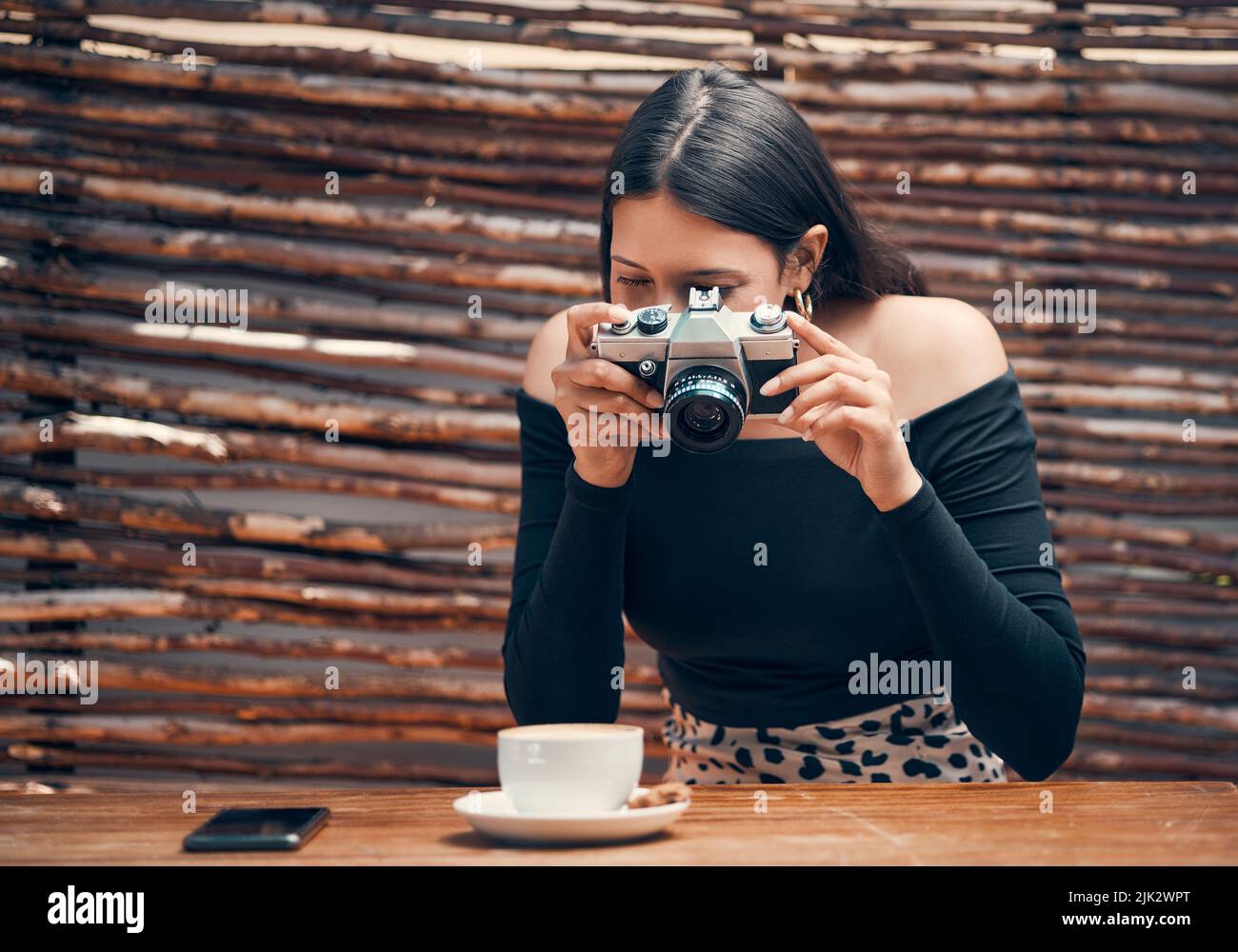 Stylische, trendige und kreative Food-Influencerin, die mit einer Kamera eine Tasse Kaffee für ihren Blog in einem Café-Shop fotografiert. Junge Frauen zufrieden Stockfoto