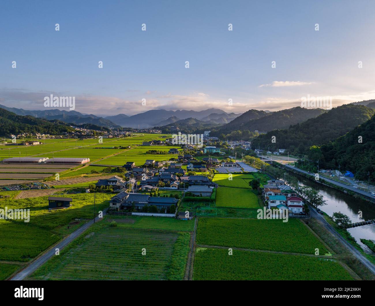 Am frühen Morgen scheint die Sonne durch Berge auf kleinen Dörfern und Reisfeldern Stockfoto