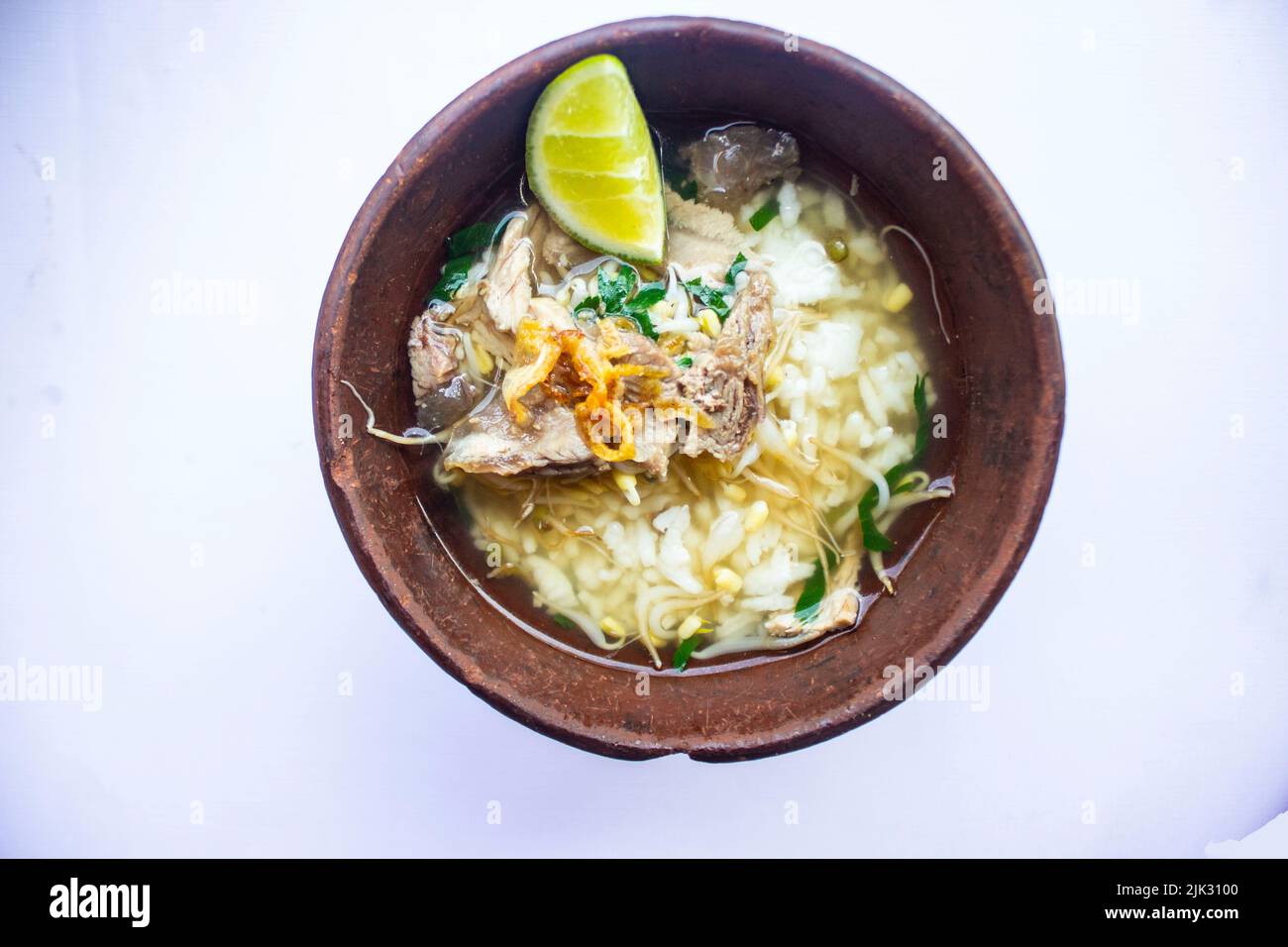 soto kwali. Isoliert auf weißem Hintergrund. Javanesische Rindfleischsuppe mit Rosenkohl, Limette und Reis; serviert in einer traditionellen Schüssel aus Kwali (ein Kon Stockfoto