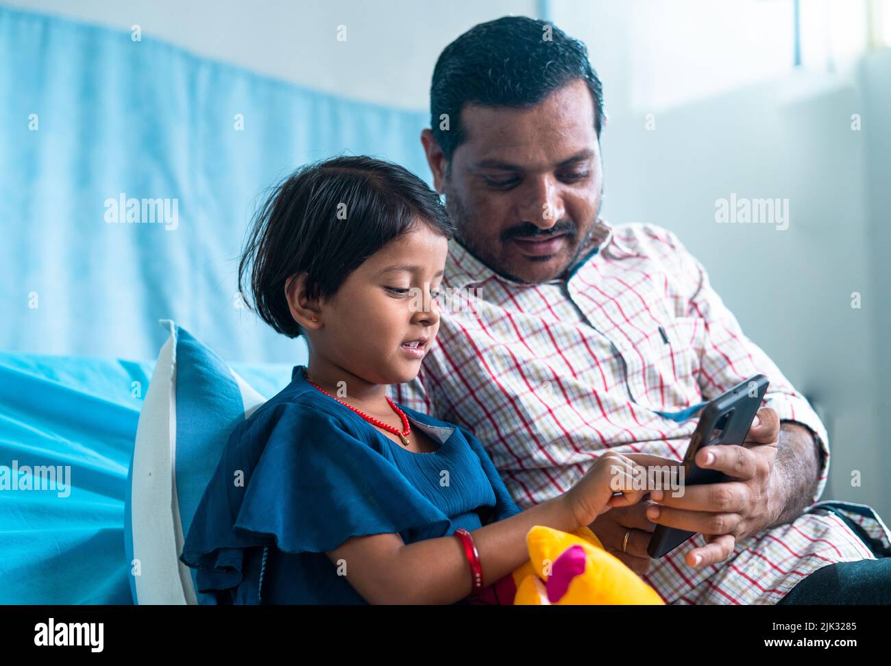 Glücklich lächelnd erholte sich Tochter mit Vater, der Videos auf dem Mobiltelefon ansah, während er auf der Krankenstation saß - Konzept der sozialen Medien, Unterstützung der Familie Stockfoto