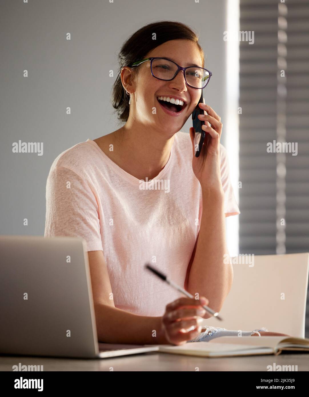 ich kann es kaum erwarten, diese Geschichte zu hören. Eine junge Frau, die mit ihrem Smartphone telefoniert, während sie von zu Hause aus arbeitet. Stockfoto