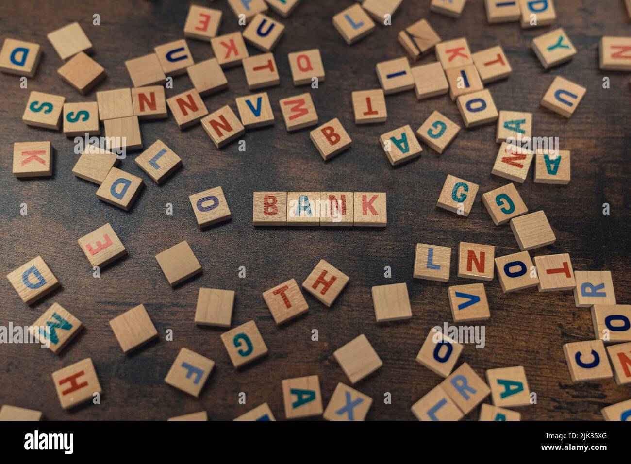 BANK. Geld- und Sparkonzept. Verstreute bunte hölzerne Buchstaben Puzzles schaffen die Wortbank. Holztisch als Hintergrund. Draufsicht. Hochwertige Fotos Stockfoto