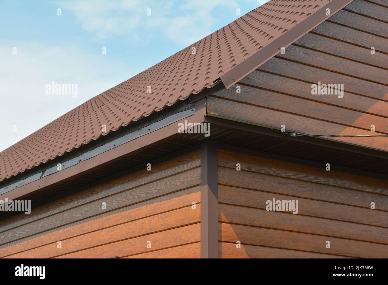 Eine Nahaufnahme einer Hausecke mit Außenverkleidungen aus Holz, Holzverkleidungen mit einer Metalldachkonstruktion ohne Dachrinne. Stockfoto