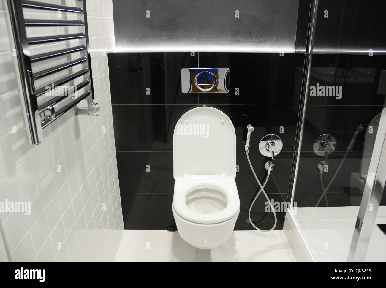 Modernes schwarz-weißes WC, Badezimmer mit wandmontierter Toilettenschüssel, Bidet-Dusche, Bidet-Sprühgerät und beheizten Handtuchhaltern, Heizkörper. Stockfoto