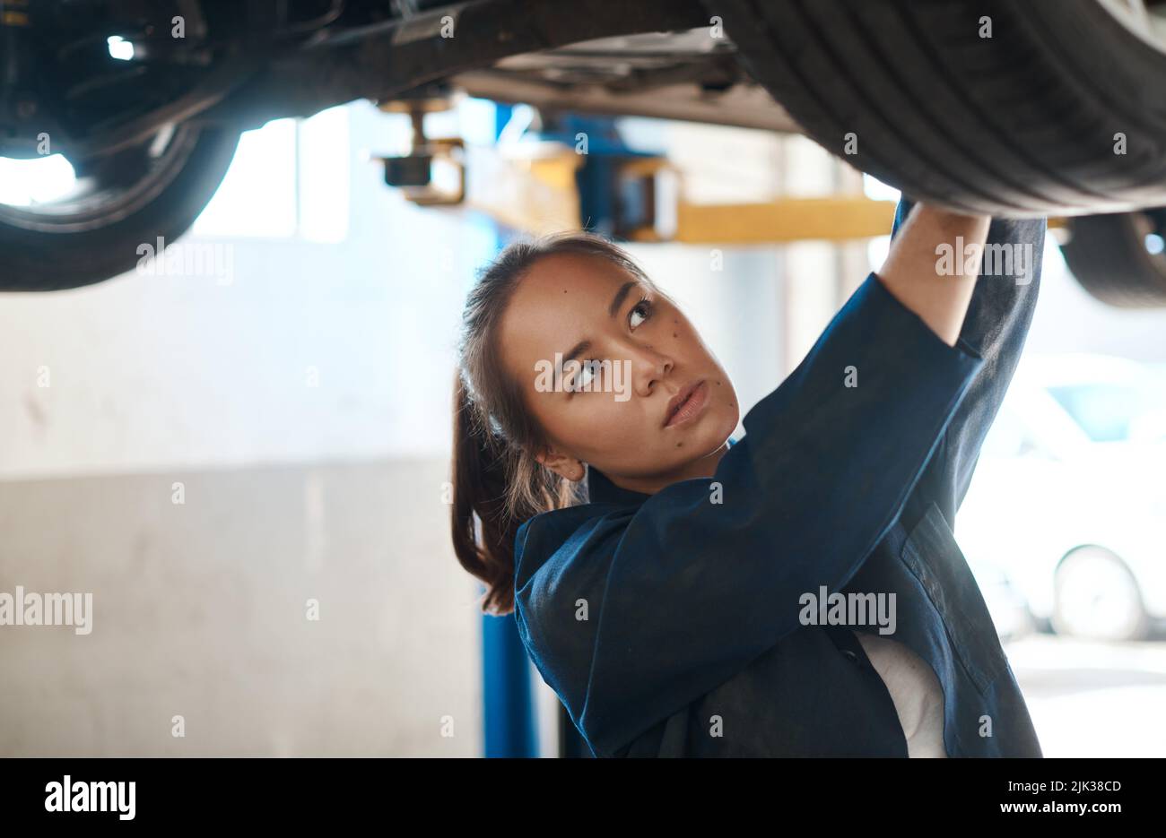 Probleme zu erkennen und Reparaturen durchzuführen, ist das, was ich tue. Eine Mechanikerin, die unter einem angehobenen Auto arbeitet. Stockfoto