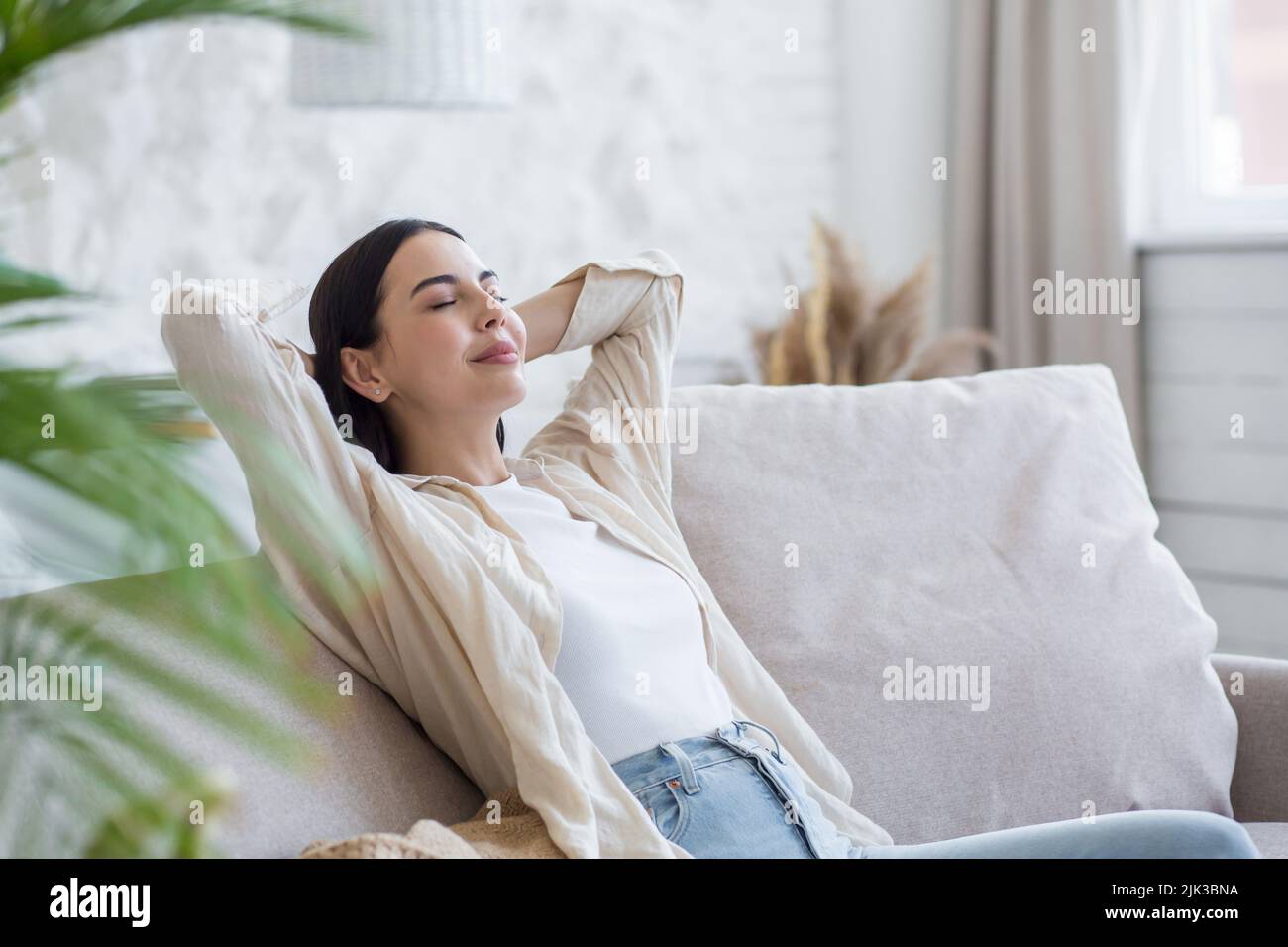 Schöne Brünette Frau, die tagsüber mit geschlossenen Augen ruht, träumte und döst zu Hause auf der Couch sitzend Stockfoto