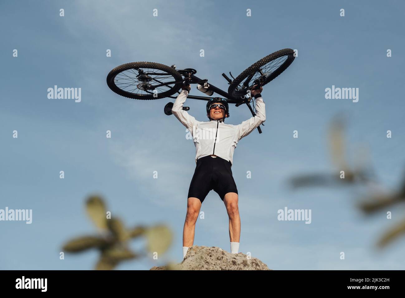 Professioneller Radsportler, der die Hände mit dem Fahrrad hebt, während er auf dem Gipfel des Hügels steht, Himmel auf dem Hintergrund Stockfoto