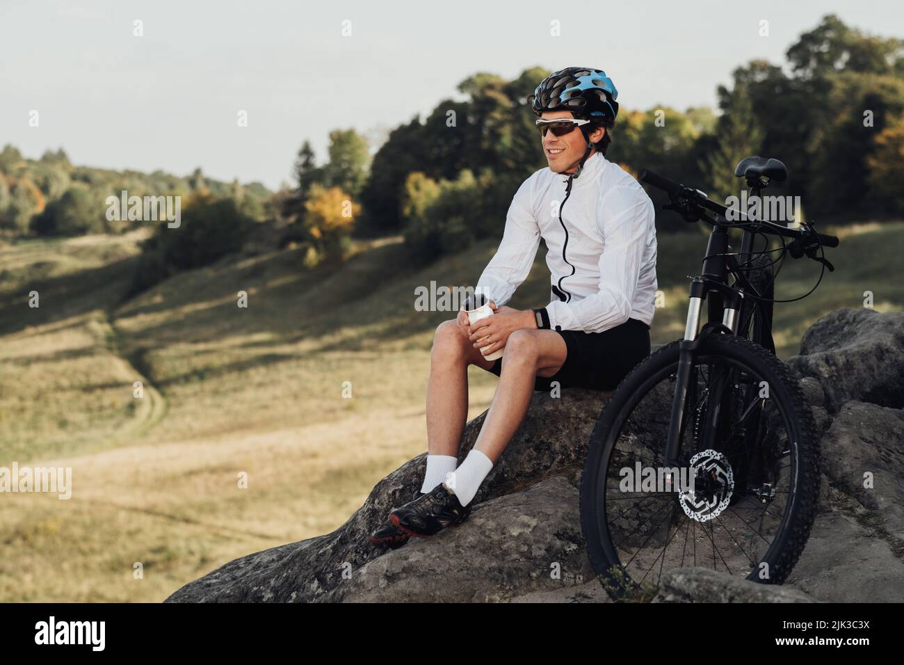 Schöner professioneller Radsportler, der mit dem Mountainbike auf dem Felsen sitzt, Erwachsener, der sein extremes Hobby mit Panoramablick genießt Stockfoto