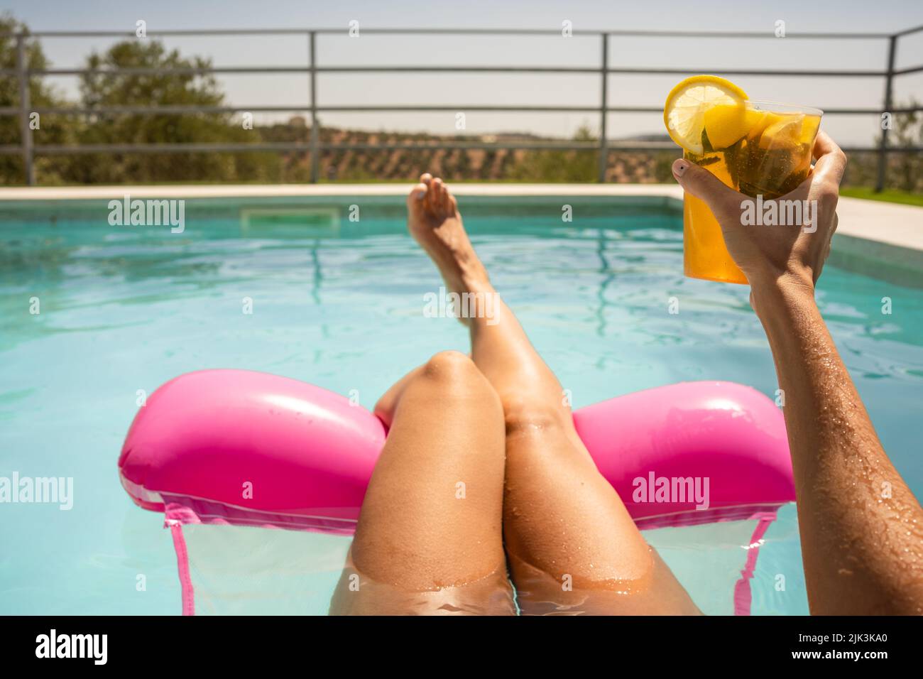 Eine glückliche Frau auf einer aufblasbaren Matratze, die im Sommer einen Mojito-Cocktail im Pool hat Stockfoto