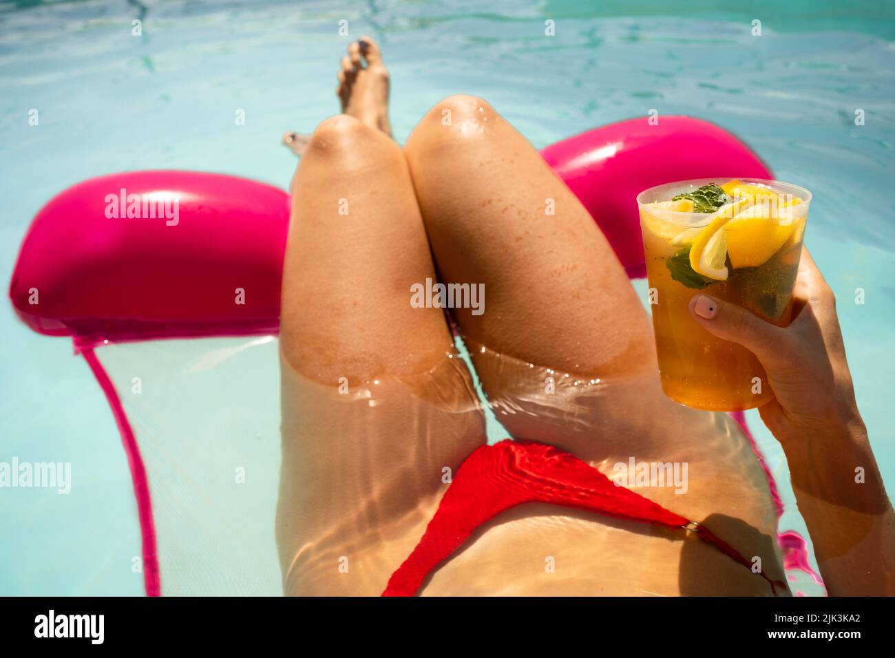 Frau in rotem Bikini auf einer aufblasbaren Matratze, die im Sommer einen Mojito-Cocktail im Schwimmbad hat Stockfoto
