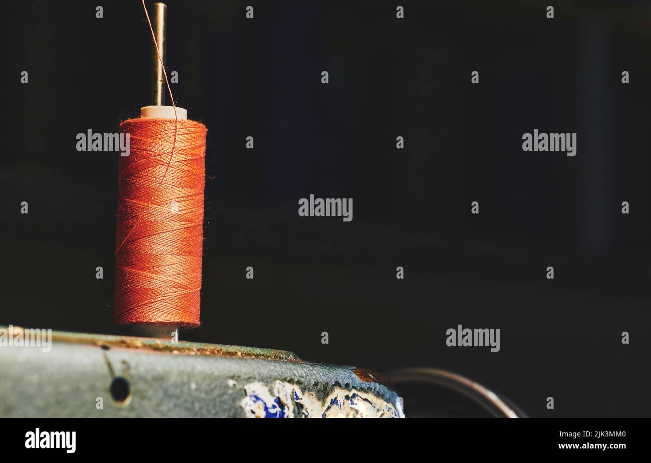 Orangefarbene Garnspule auf einer alten grauen Nähmaschine und einem dunklen Hintergrund Stockfoto