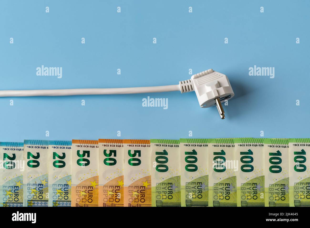 Netzstecker über der Reihe der Euro-Geldscheine auf blauem Hintergrund. Konzept der steigenden Energiekosten und Strompreisspitzen. Hohe Energiekosten. Stockfoto