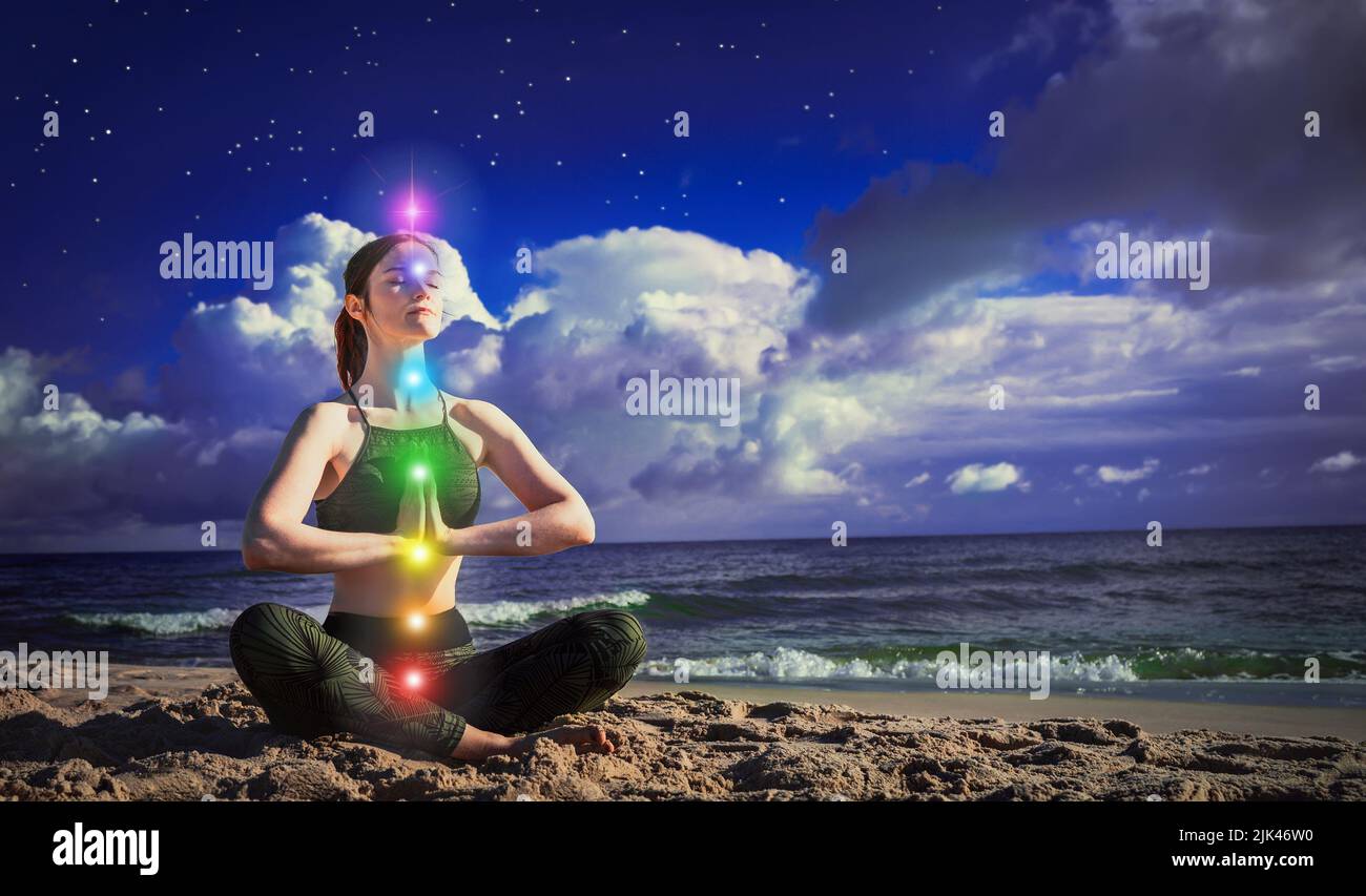 7 Chakren. Eine Frau meditiert in der Lotusposition auf dem Hintergrund des dunkelblauen Himmels und des Meeres. Das Konzept von Harmonie und Heilung. Ruhig Stockfoto