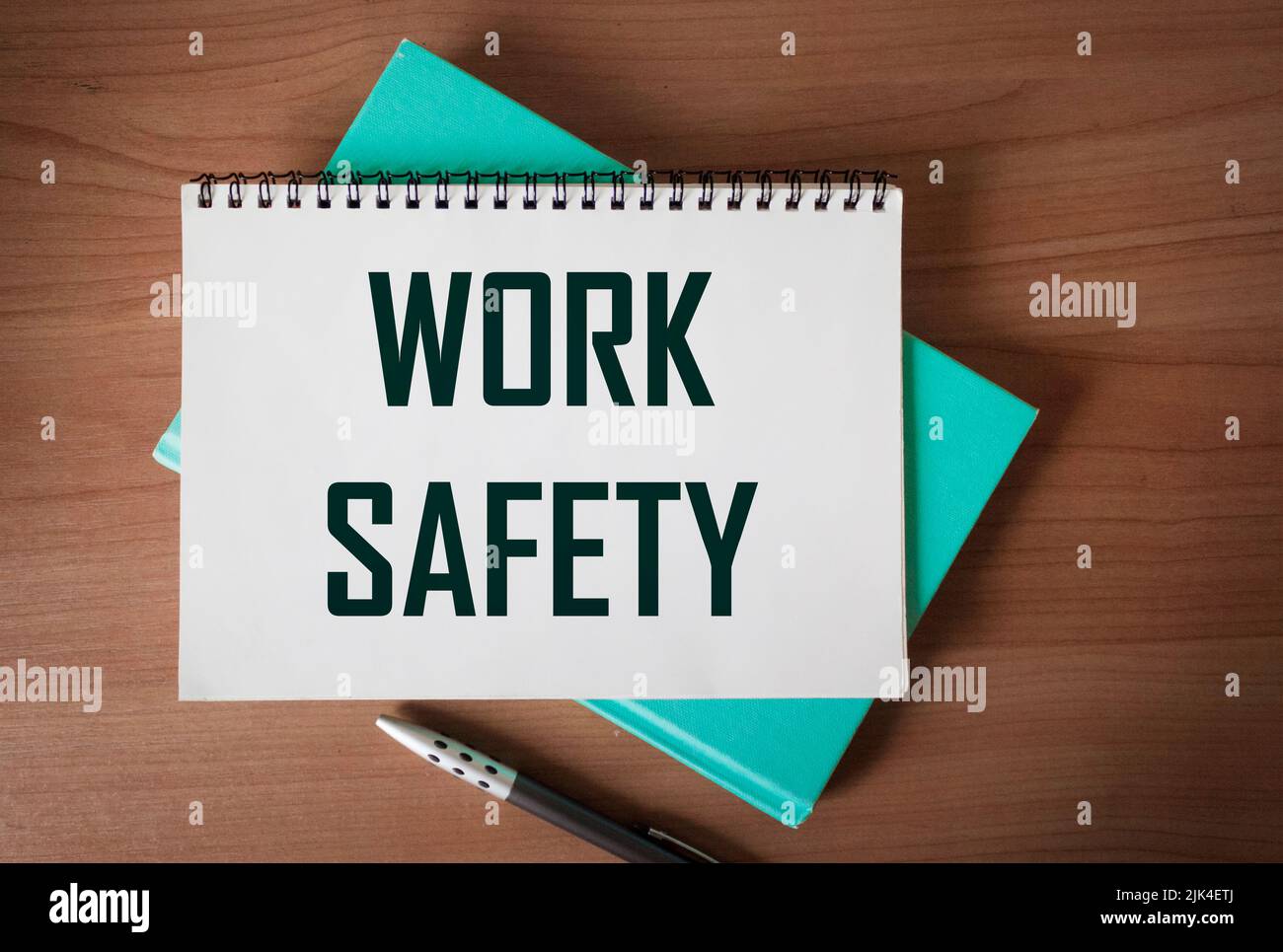Weiße Karte mit dem Text ARBEITSSICHERHEIT auf einem Holzarbeitstisch mit einem grünen Tagebuch. Flache Verlegung des Arbeitsplatzes. Stockfoto