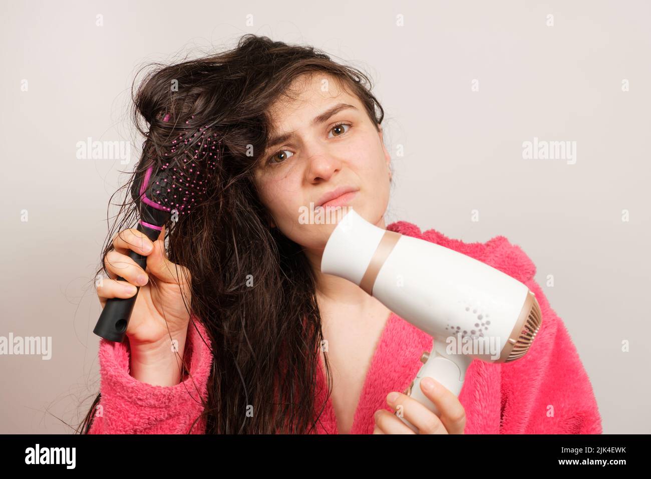 Eine Brünette mit mattierten Haaren trocknet es mit einem Haartrockner. Haarpflege, übertrocknetes Haar Stockfoto