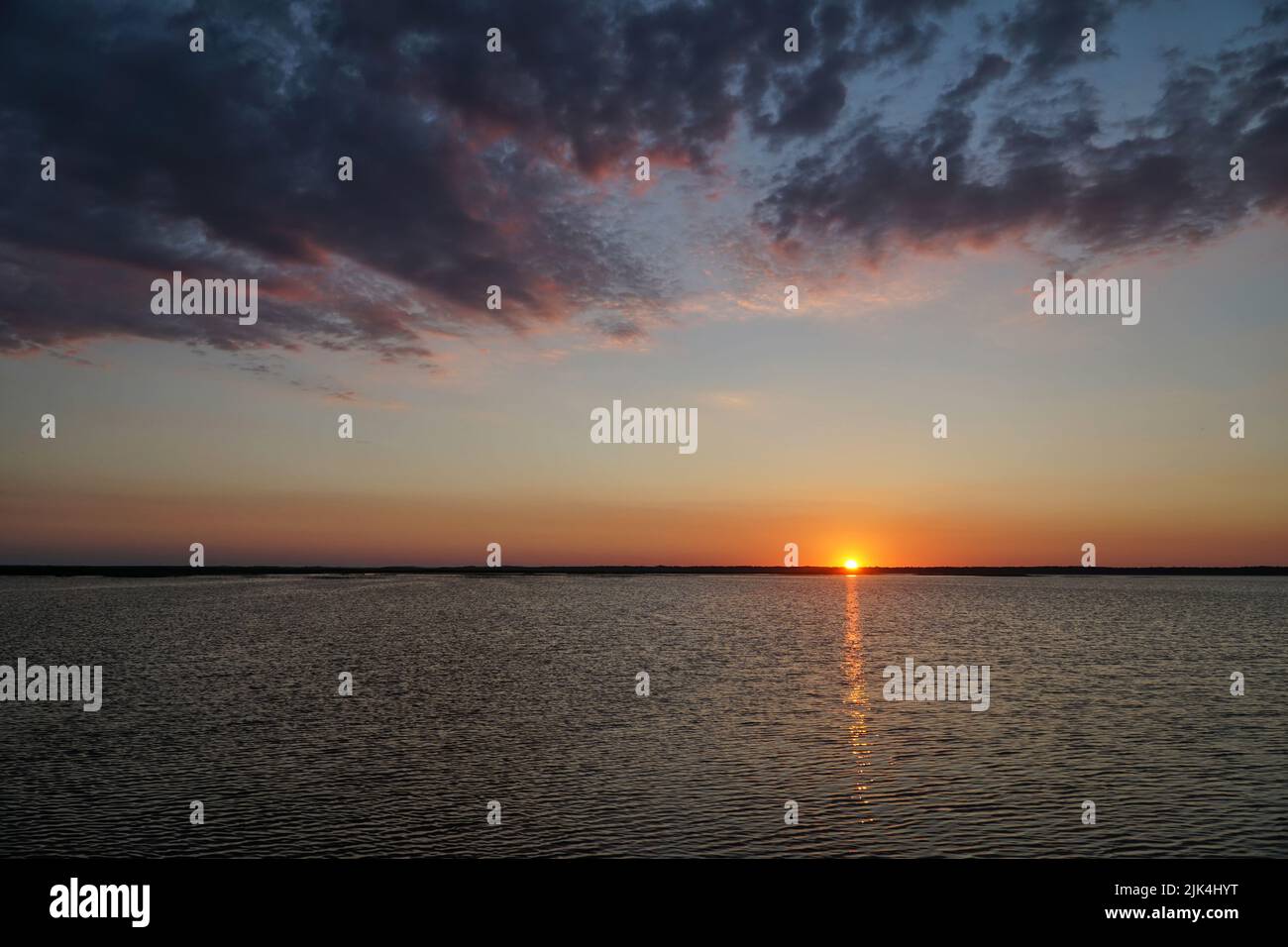 Sonnenuntergang am Łebsko-See, Woiwodschaft Pommern, Polen. Sommerabend, dramatische dunkle Wolken am Himmel, die Sonne versteckt sich hinter dem Horizont, die Refl Stockfoto