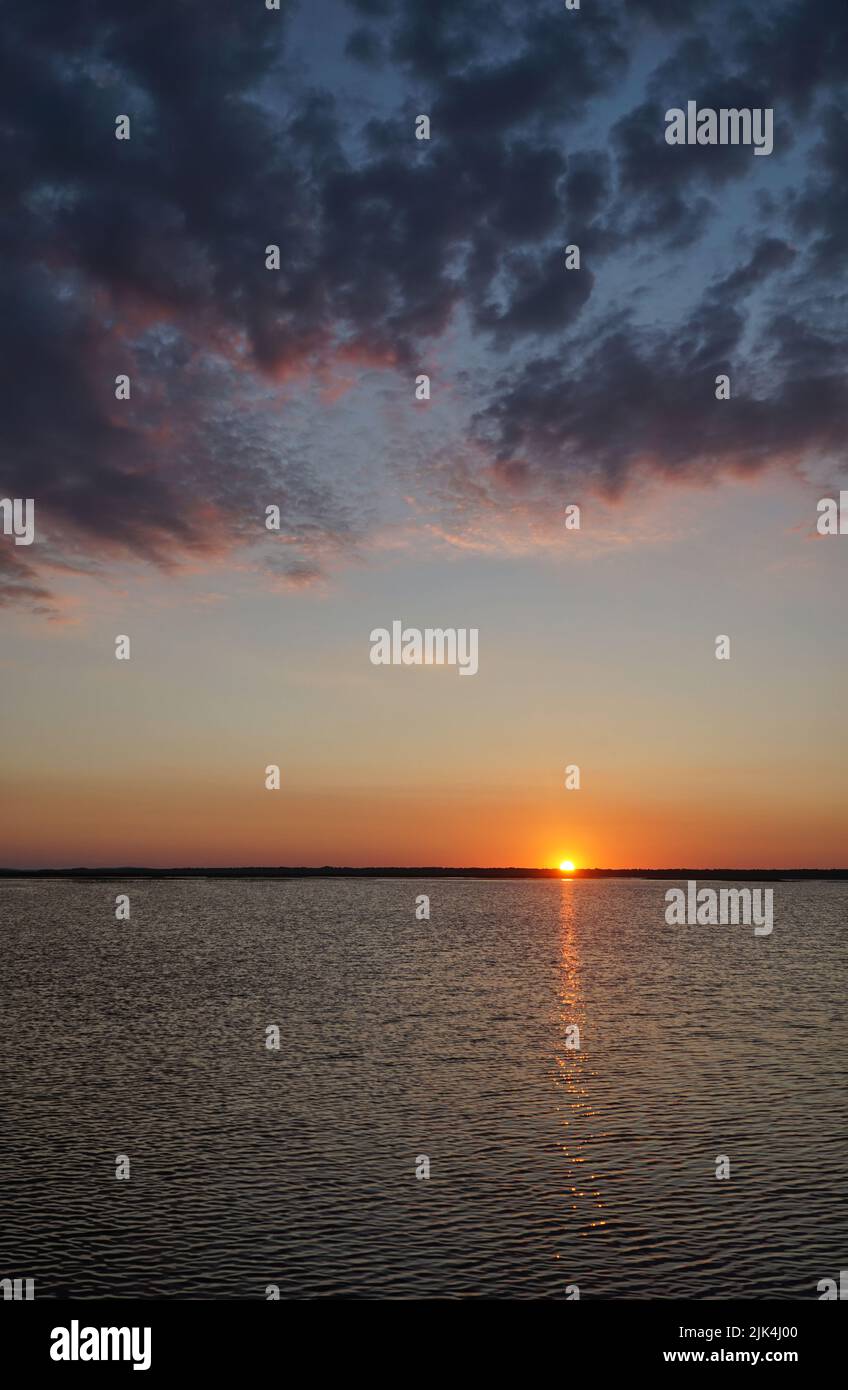 Sonnenuntergang am Łebsko-See, Woiwodschaft Pommern, Polen. Sommerabend, dramatische dunkle Wolken am Himmel, die Sonne versteckt sich hinter dem Horizont, die Refl Stockfoto