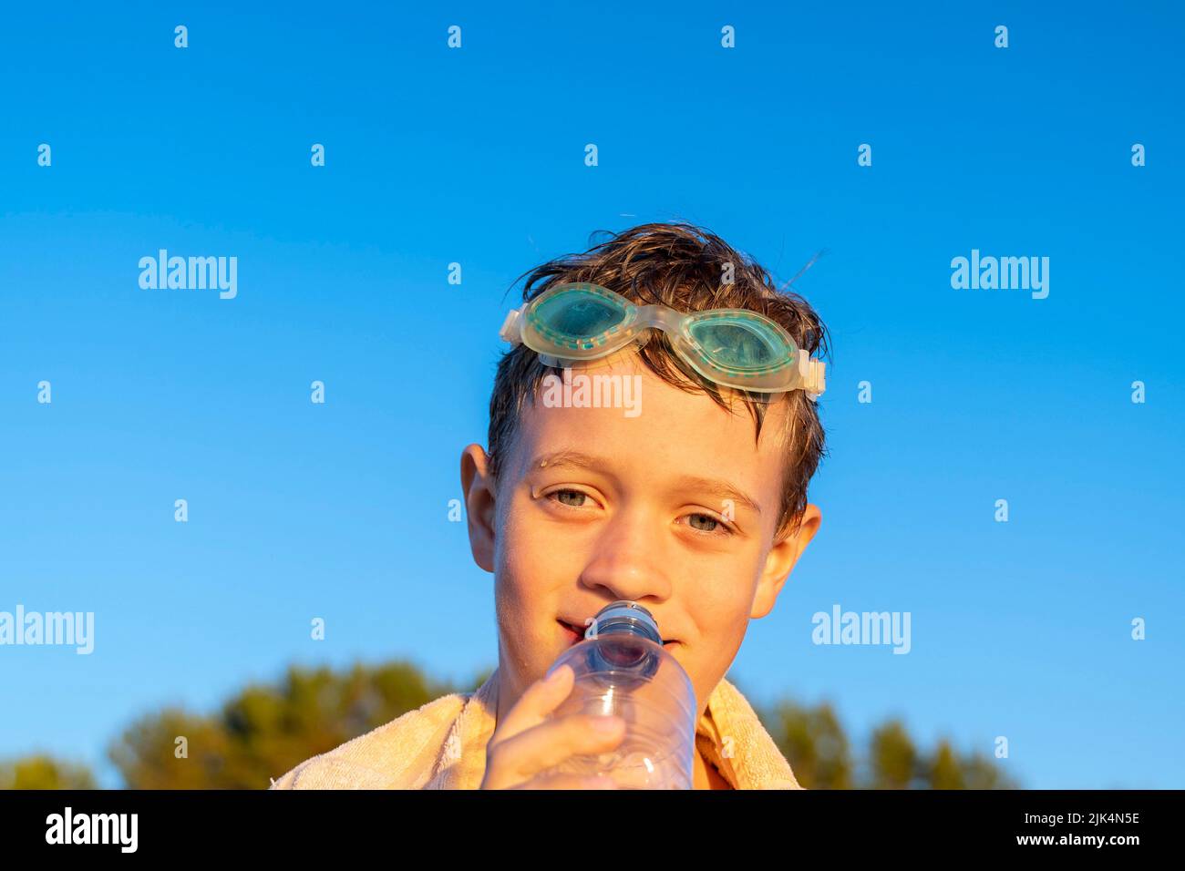 Glücklicher Junge in den Schwimmgläsern trinkt Wasser aus einer Flasche am Strand Stockfoto