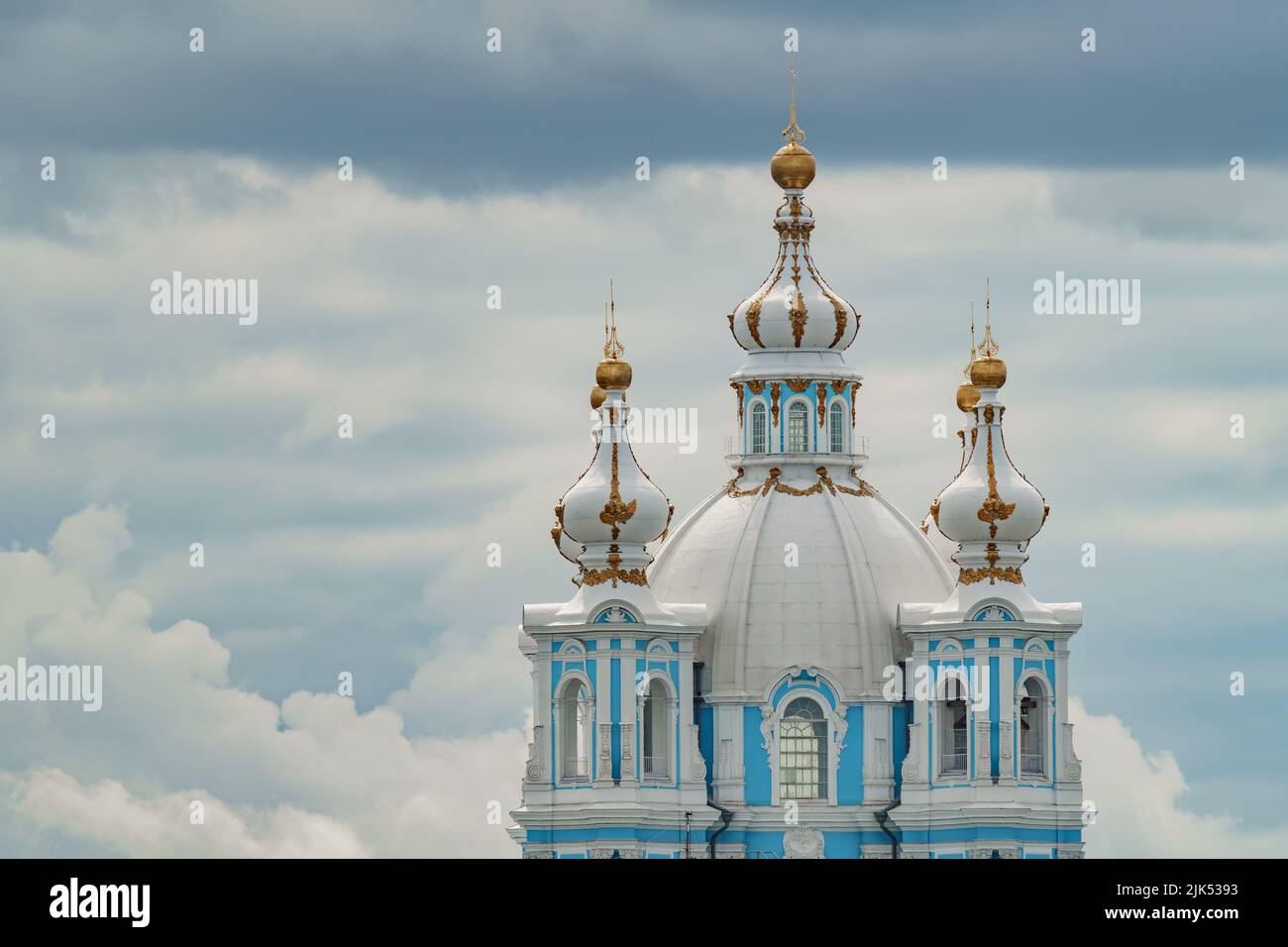 goldene Kuppeln und Kreuze der Smolny-Kathedrale bei sonnigem Wetter vor dem Hintergrund eines düsteren Himmels Stockfoto