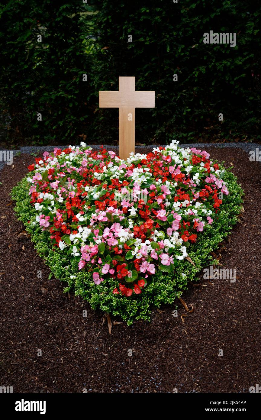 Bunte herzförmige Blumenarrangements auf einem Grab mit Holzkreuz Stockfoto