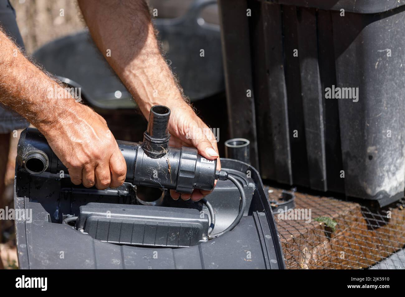 Ein UV-Klärer, der von kaukasischen männlichen Händen bei Sonnenlicht aus einem Koi-Teichfiltersystem entfernt wird Stockfoto