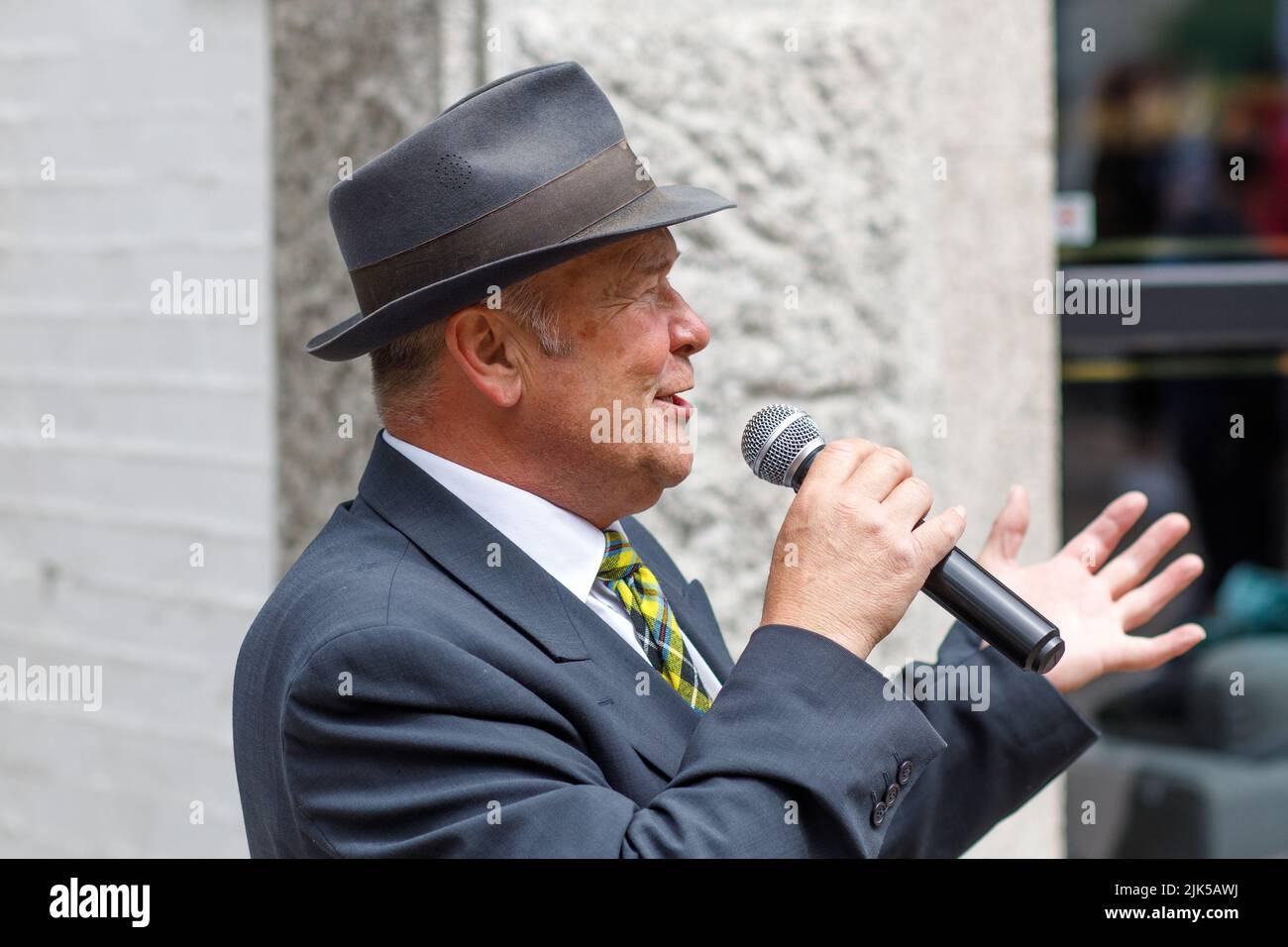 Ein männlicher Straßenmusiker mit blauem Anzug im Stil der 40er Jahre, dreibiger Krawatte und gelber Krawatte, der in einer Straße in Newquay, Großbritannien, singt Stockfoto