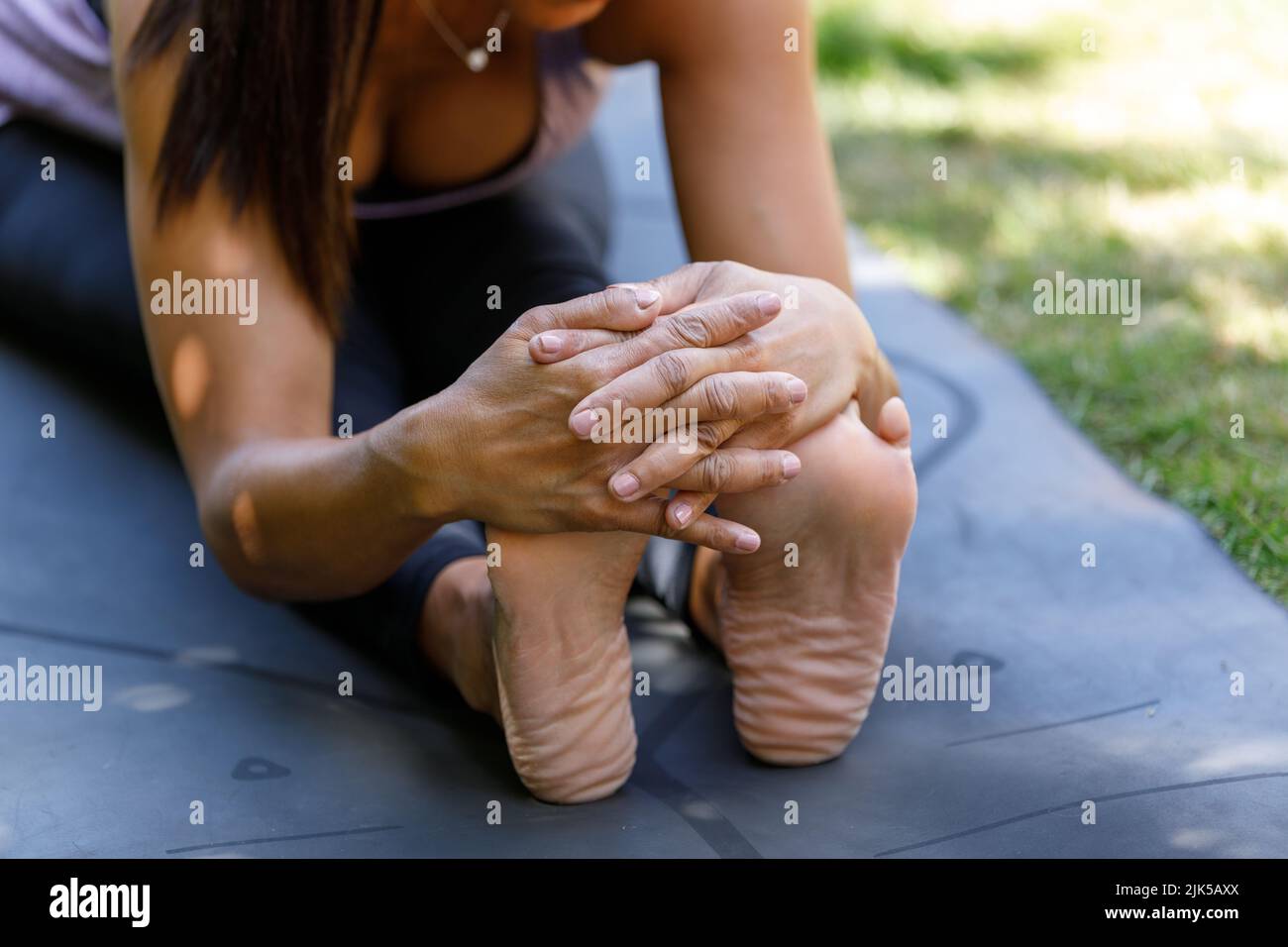 Nahaufnahme einer Frau, die in einer Yoga-Pose mit Vorwärtsbeuge sitzt. Eine Dame streckt ihre Füße und ihre Hamstrings mit ihren Händen in der Paschimottanasana Yoga-Pose. Stockfoto