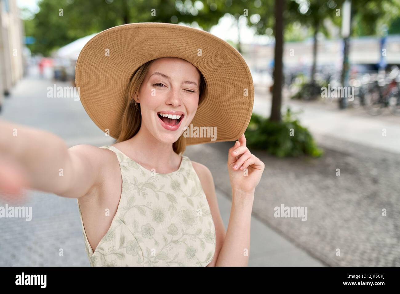 Junge glückliche Frau mit Hut winken beim Selfie auf der Straße der Sommerstadt. Stockfoto