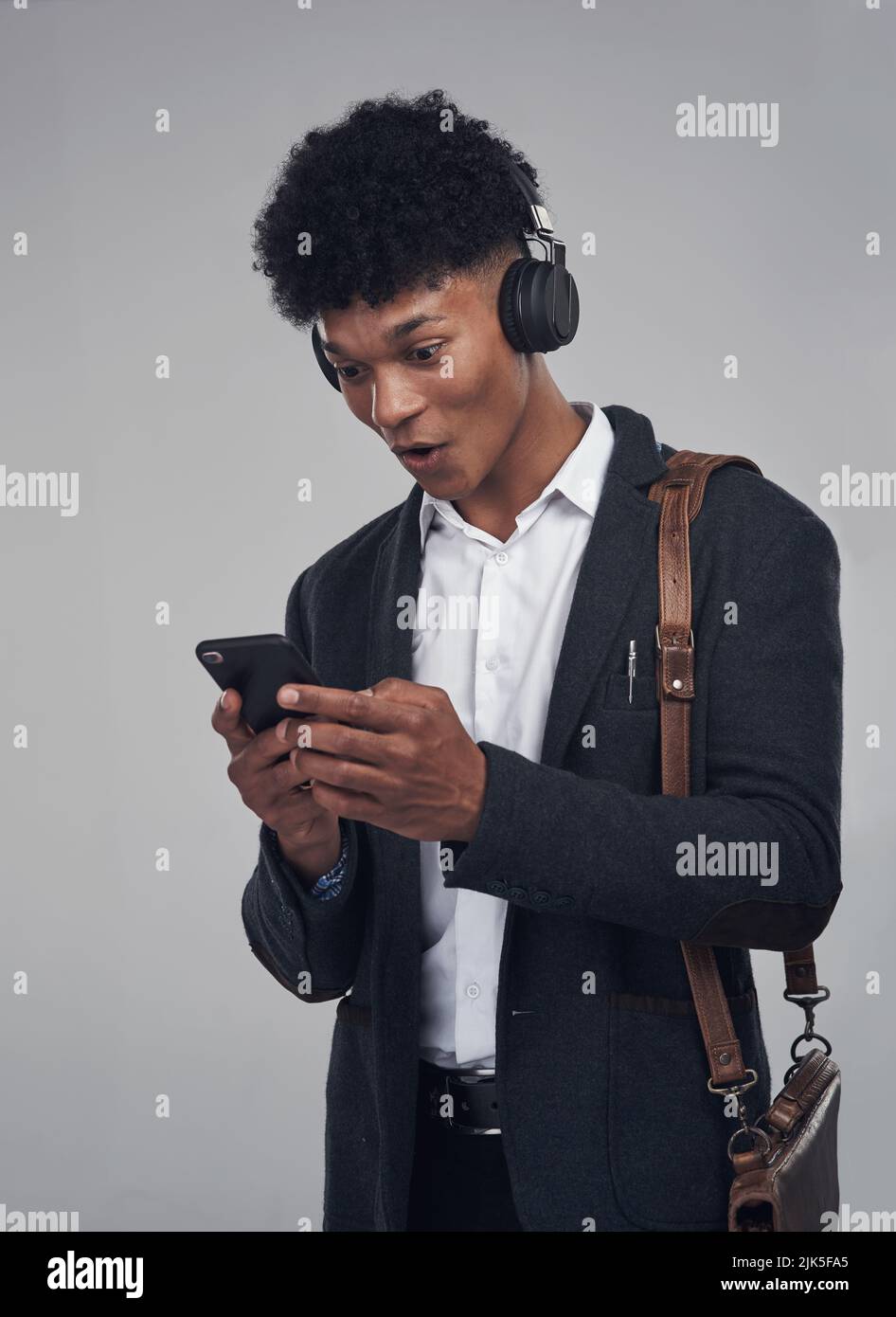 Drehen Sie es auf und lassen Sie die Musik ihren Zauber entfalten. Studioaufnahme eines jungen Geschäftsmannes mit Smartphone und Kopfhörer vor grauem Hintergrund. Stockfoto