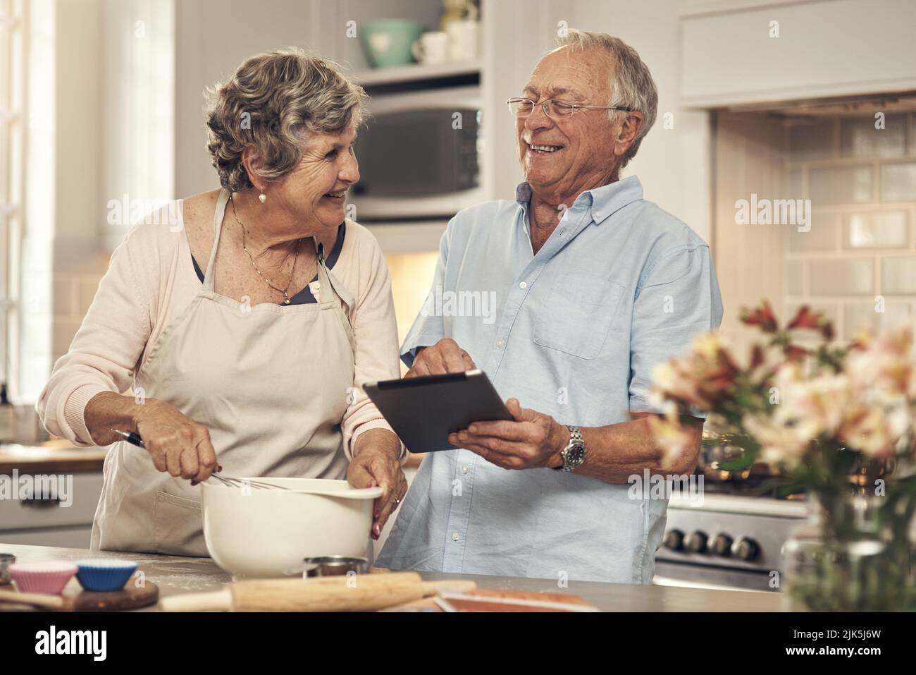 Das wird so viel Spaß machen. Ein Seniorenpaar mit einem digitalen Tablet beim Backen zu Hause. Stockfoto