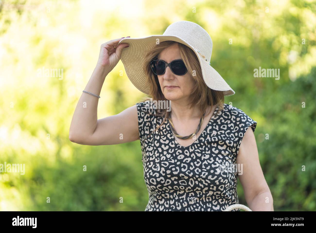 Reife Frau in einem öffentlichen Park, die an einem heißen Sommertag einen Strohhut trägt. Stockfoto