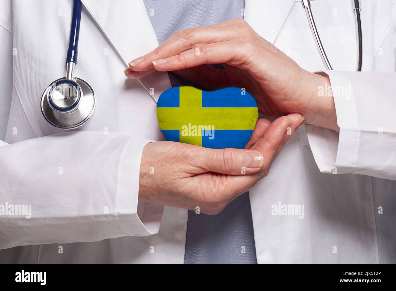 Schwedischer Arzt hält Herz mit Flagge von Schweden Hintergrund. Healthcare, Charity, Versicherung und Medizin Konzept Stockfoto