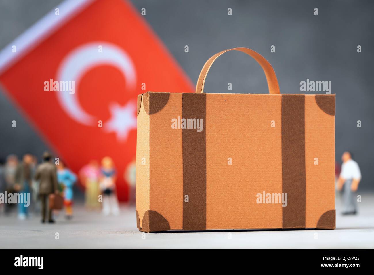 Pappkoffer, Plastikspielzeug Menschen und eine Flagge auf abstraktem Hintergrund, ein Konzept zum Thema Umzug oder Migration in die Türkei Stockfoto