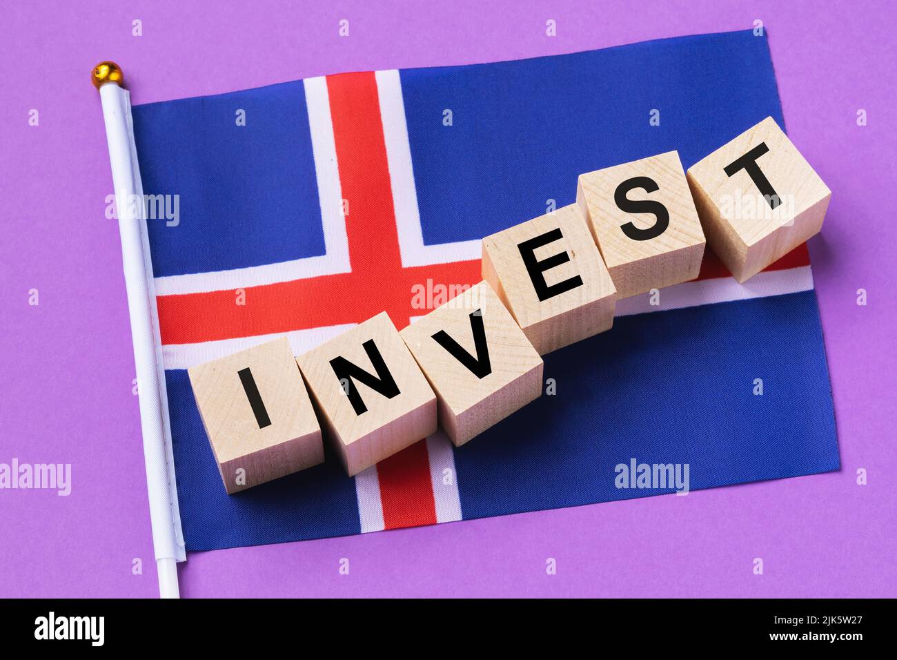 Holzwürfel mit Text und einer Flagge auf farbigem Hintergrund, das Konzept der Investition aus Island Stockfoto