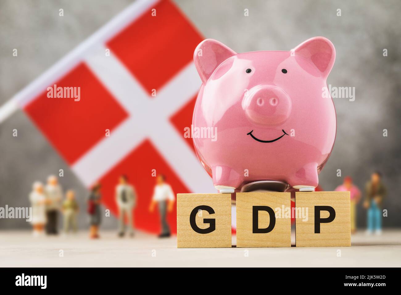 Sparschwein, Holzwürfel mit Text, Spielzeugleute aus Kunststoff und eine Fahne auf abstraktem Hintergrund, ein Konzept zum Thema schwedisches BIP Stockfoto