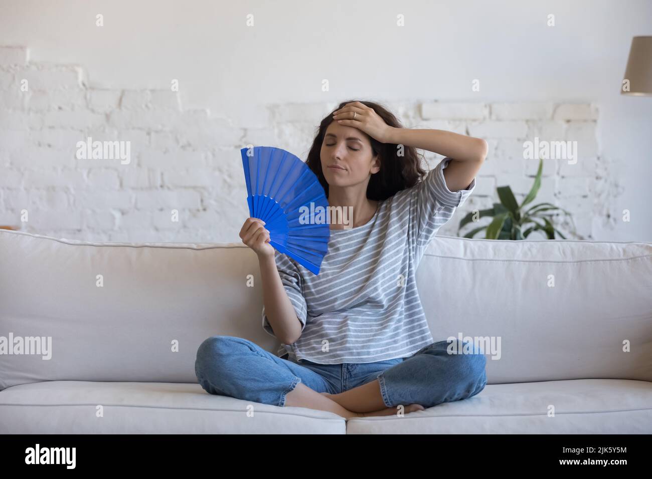 Müde Lateinerin schwenkt Handventilator aus Papier, um die Luft zu kühlen Stockfoto