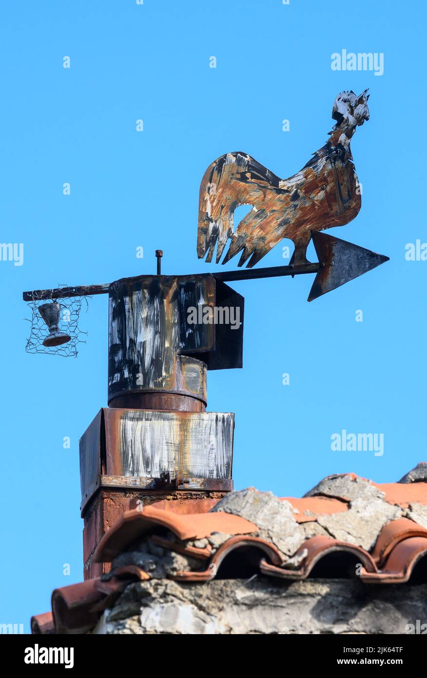 Metallschornsteintopf und Wetterfahne in Form eines krähendes Hahns auf einem Haus im kleinen Dorf Agios Germanos in der Nähe des Prespa-Sees in der Vorzeit Stockfoto